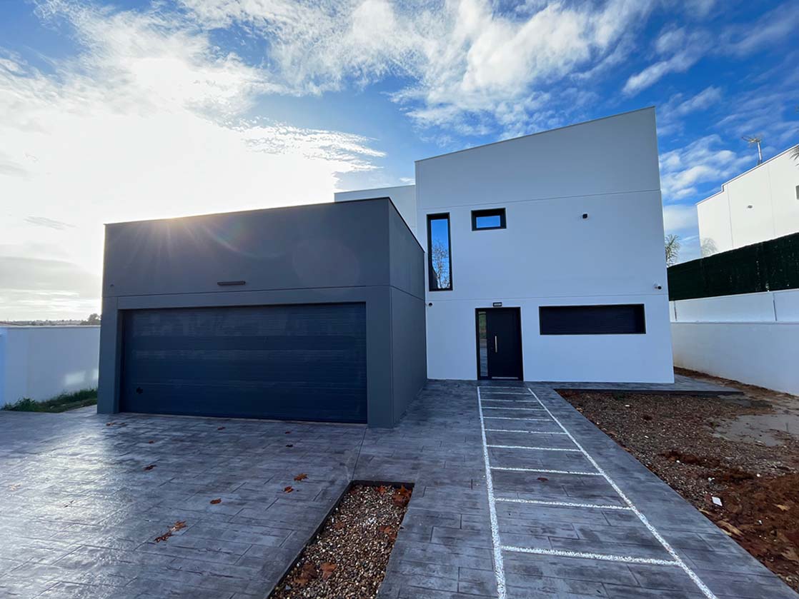Casa prefabricada de hormigón terminada, con garaje en volumen gris y fachada blanca